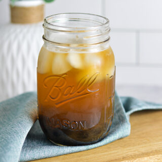 A ball mason jar filled with Honey Green Bubble Tea, with ice cubes floating on top and chewy tapioca pearls at the bottom of the glass.