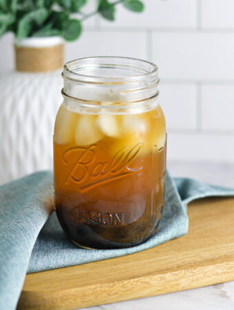 A ball mason jar filled with Honey Green Bubble Tea, with ice cubes floating on top and chewy tapioca pearls at the bottom of the glass.