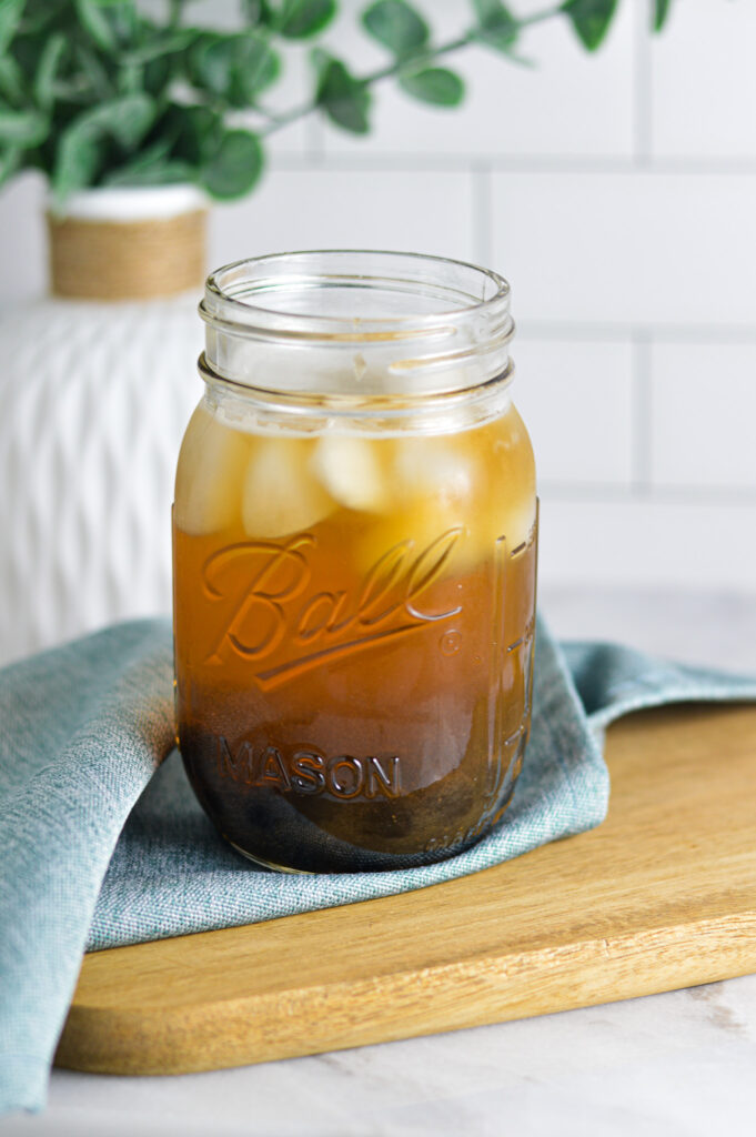 A ball mason jar filled with Honey Green Bubble Tea, with ice cubes floating on top and chewy tapioca pearls at the bottom of the glass.