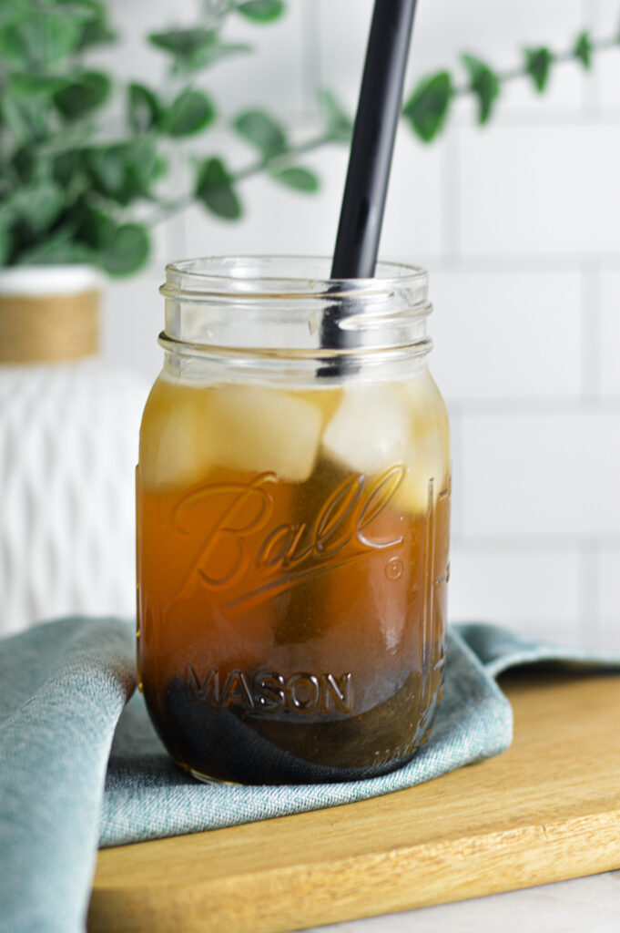 A black straw coming out of a mason jar filled with ice cold Honey Green Bubble Tea, toped by cubed ice.