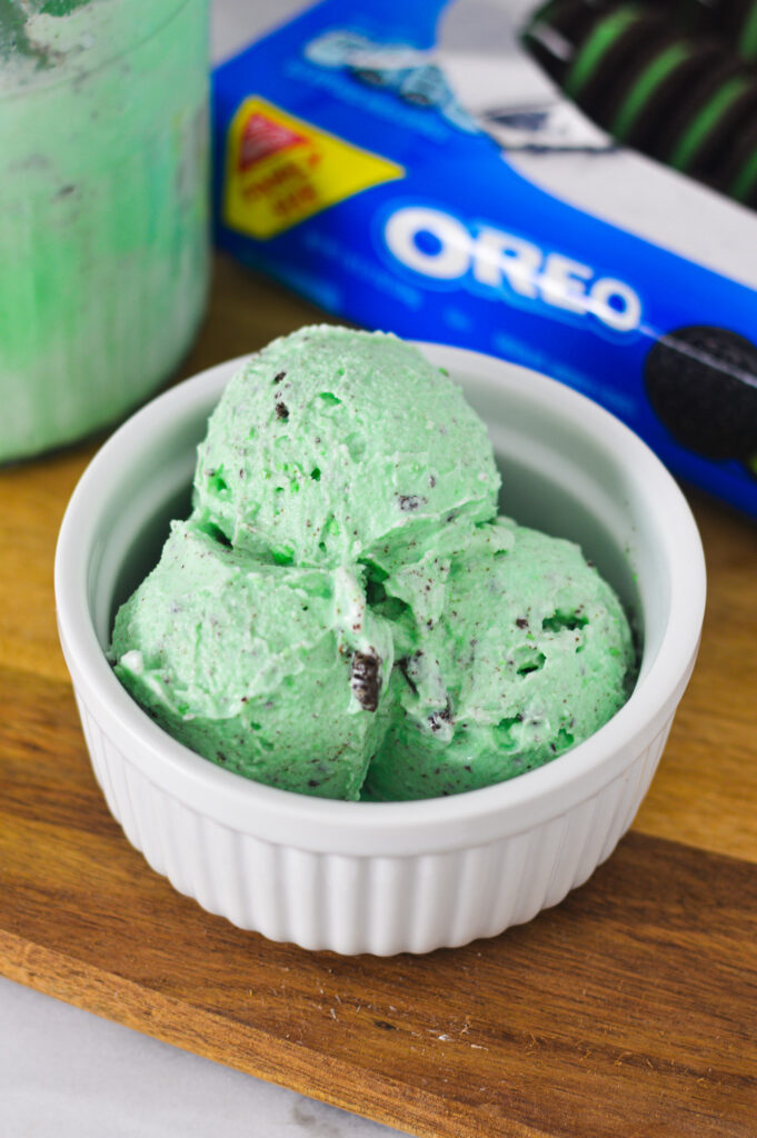 A bowl of Ninja Creami Mint Oreo Ice Cream with a container of Mint Oreos and the Ninja Creami pint in the background.