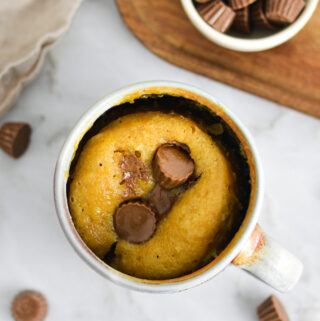 A warm Peanut Butter Cup Mug Cake, with mini Reese's peanut butter cups melted into the fluffy single serve cake.