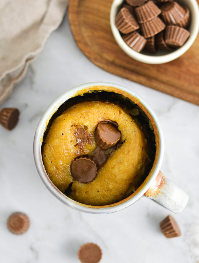 A warm Peanut Butter Cup Mug Cake, with mini Reese's peanut butter cups melted into the fluffy single serve cake.