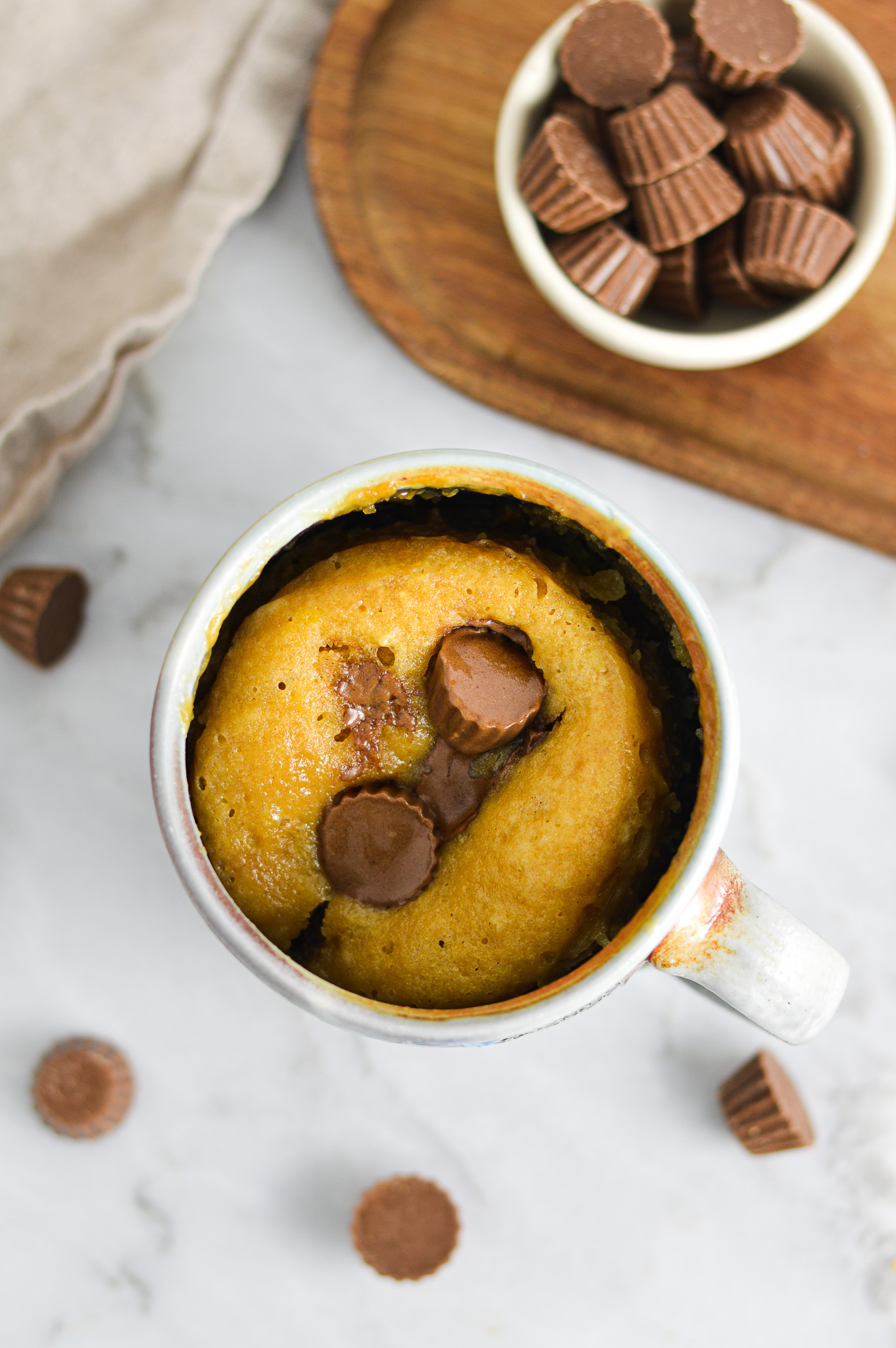 A warm Peanut Butter Cup Mug Cake, with mini Reese's peanut butter cups melted into the fluffy single serve cake.