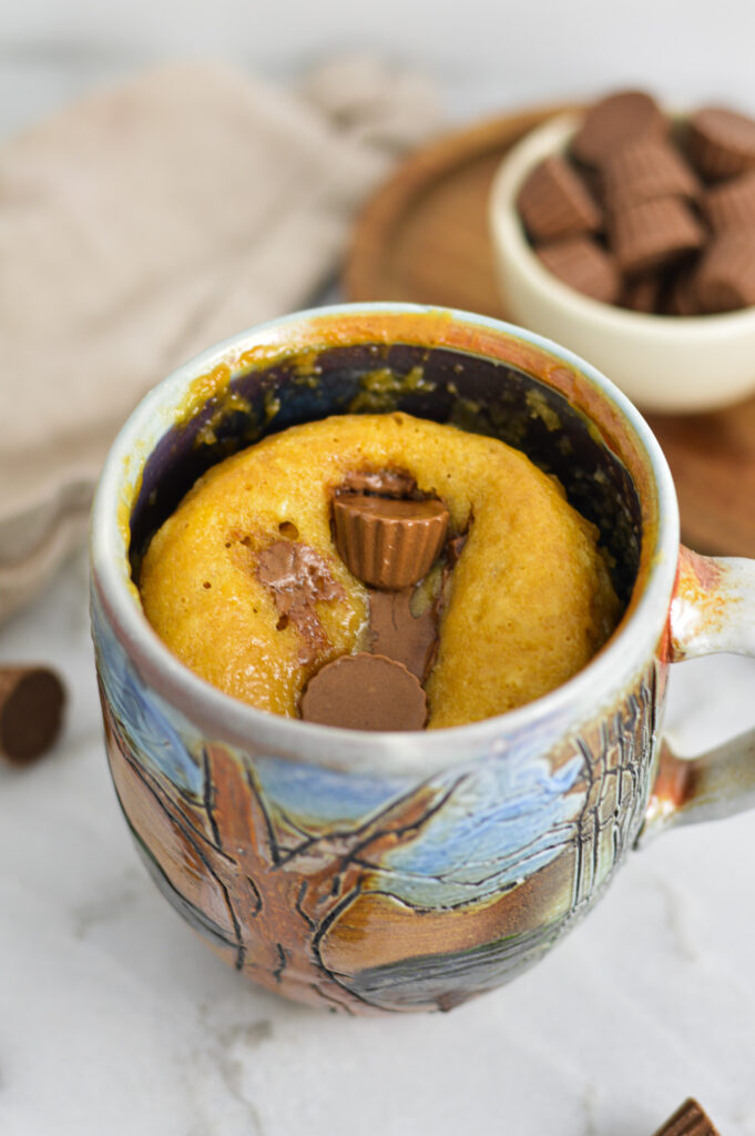 A fluffy Peanut Butter Cup Mug Cake, with melted chocolate from the mini peanut butter cups imbedded into the soft peanut butter cake.