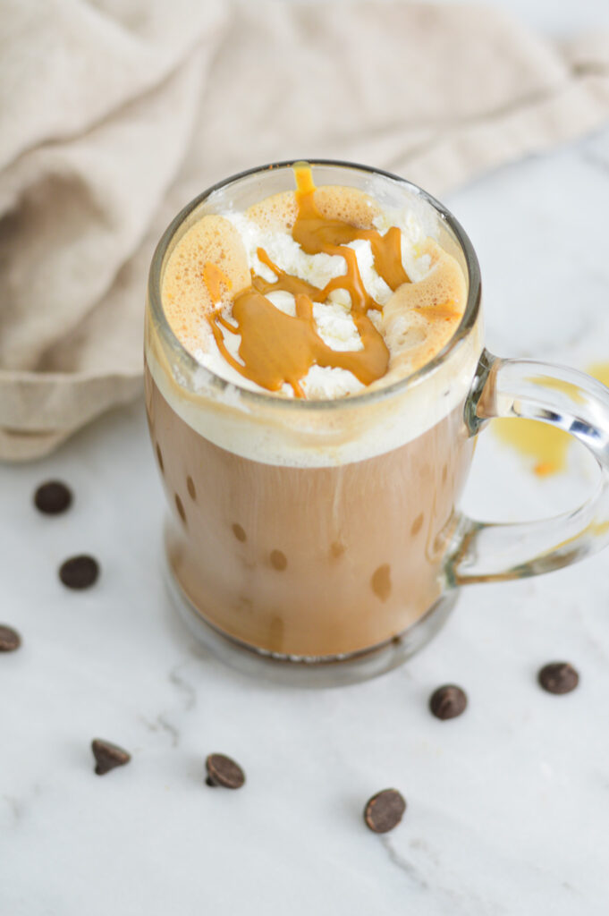 A glass stein filled with Peanut Butter Mocha, with whipped cream and creamy peanut butter on top, surrounded by chocolate chips.