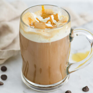 A mug filled with Peanut Butter Mocha topped with whipped cream and peanut butter drizzle, surrounded by semi-sweet chocolate chips.