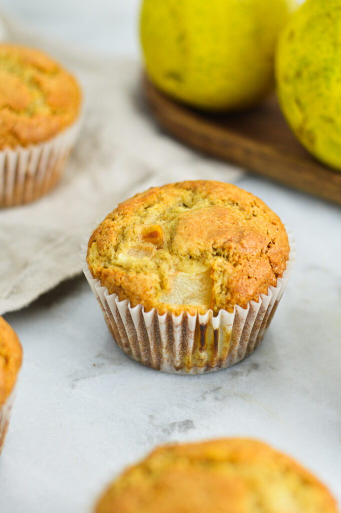 Fluffy pear muffins in paper liners, with some green pears on a wooden board in the background.