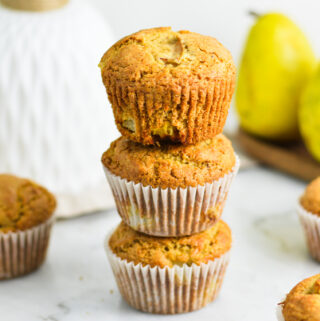 A stack of Pear Muffins, with the paper muffin cup removed from the top muffin, showing its golden brown exterior.