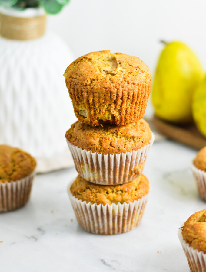 A stack of Pear Muffins, with the paper muffin cup removed from the top muffin, showing its golden brown exterior.