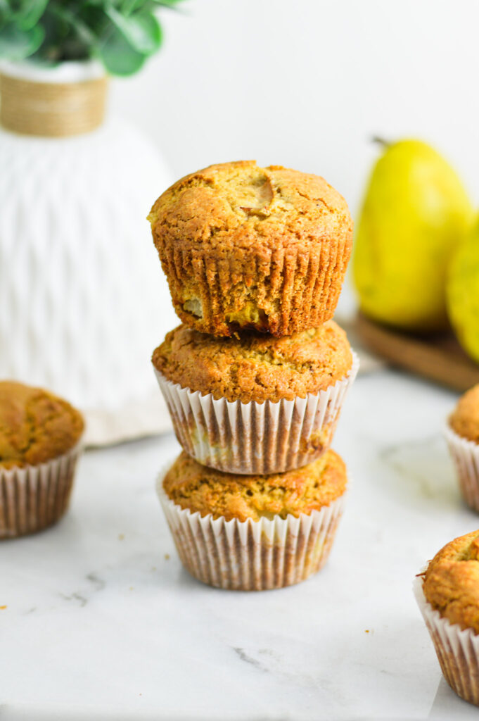 A stack of Pear Muffins, with the paper muffin cup removed from the top muffin, showing its golden brown exterior.