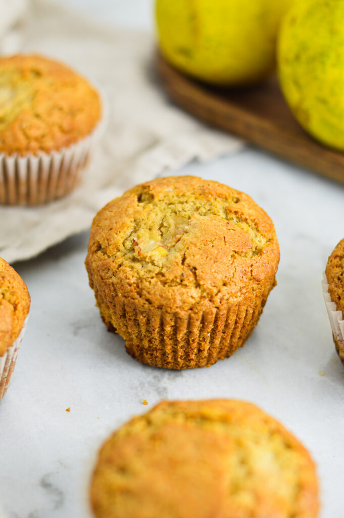 Pear Muffins on a white granite surface, with some fresh pears in the background.