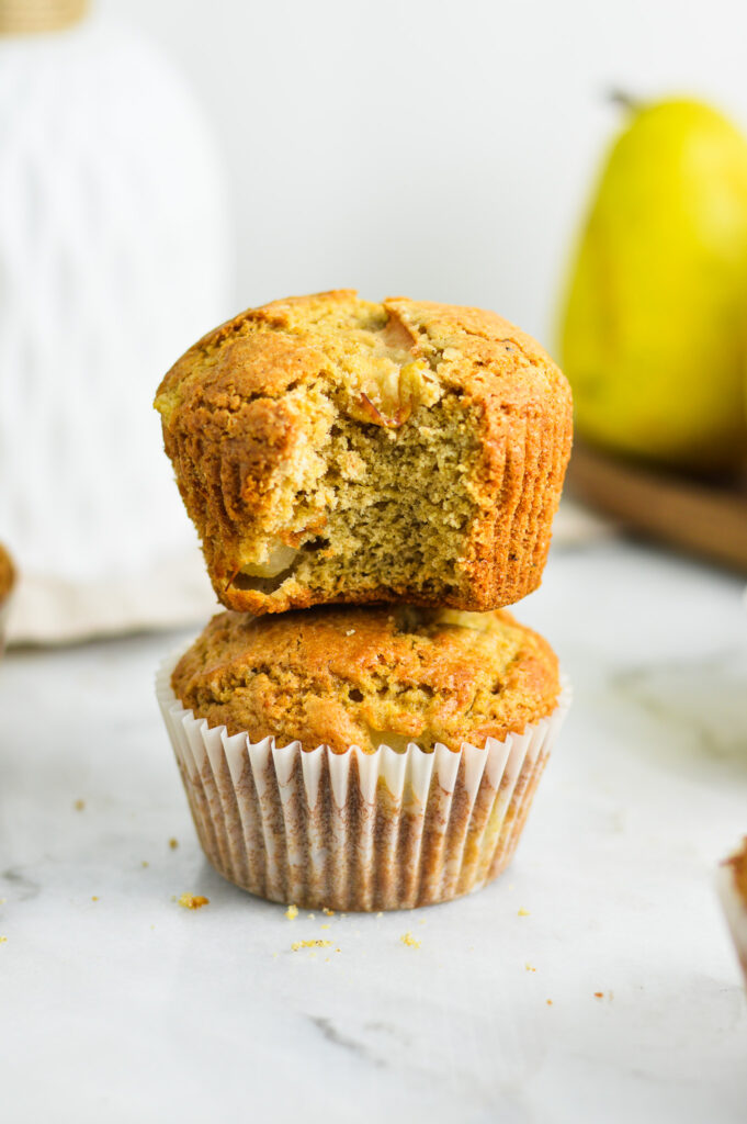 A stack of Pear Muffins, with a bite taken out of the top muffin, revealing its soft and fluffy interior.