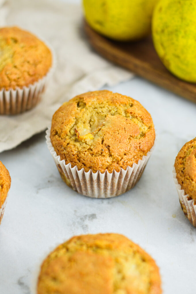 Pear Muffins with paper liners, with chunks of pear bursting out of the golden brown tops.