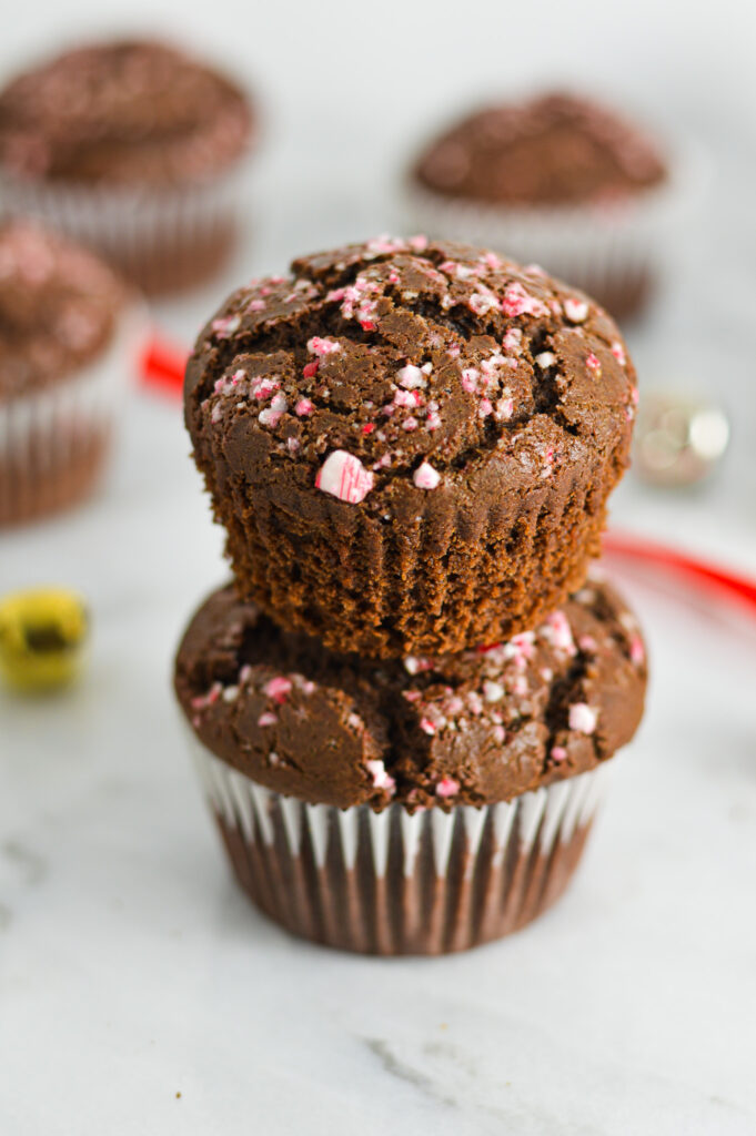 A stack of Peppermint Creamer Chocolate Muffins with the cupcake liner removed from the top muffin showing the fluffy texture.