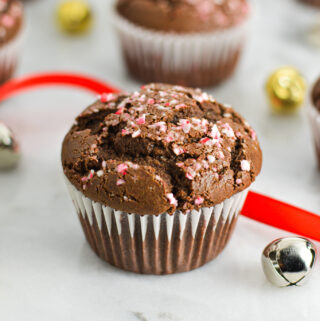 Peppermint Creamer Chocolate Muffins with crushed candy canes on top, and bells and wrapping ribbon in the background giving it a festive feel.