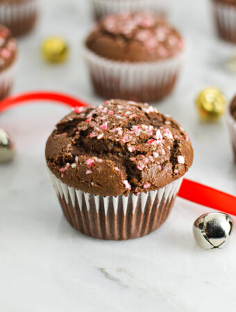 Peppermint Creamer Chocolate Muffins with crushed candy canes on top, and bells and wrapping ribbon in the background giving it a festive feel.