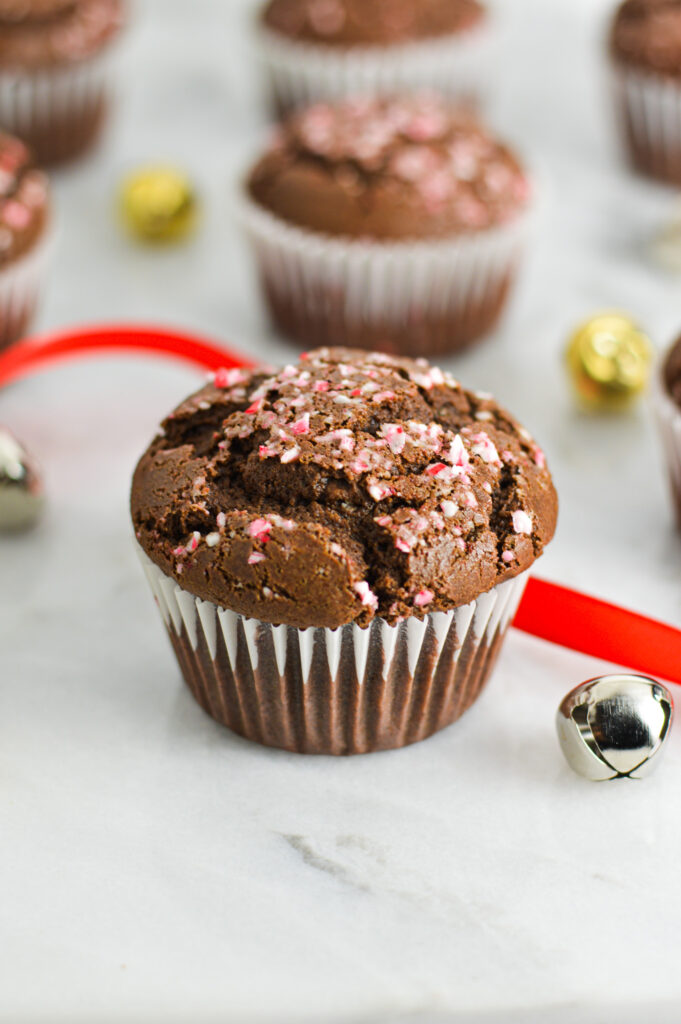 Peppermint Creamer Chocolate Muffins with crushed candy canes on top, and bells and wrapping ribbon in the background giving it a festive feel.