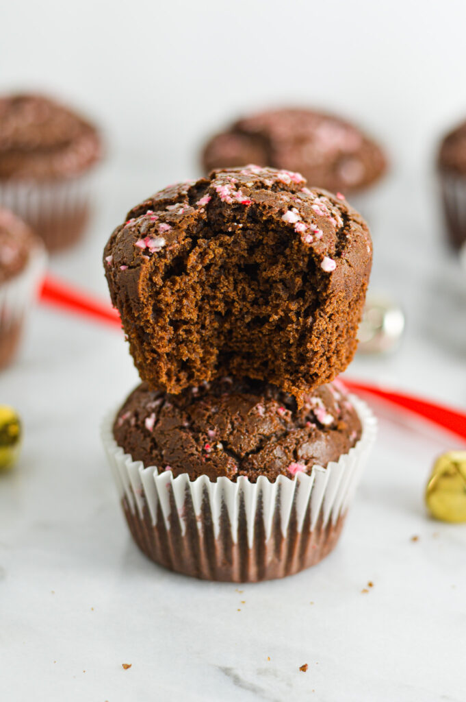 A stack of Peppermint Creamer Chocolate Muffins, with a bite taken out of the top one showing the soft texture on the inside.