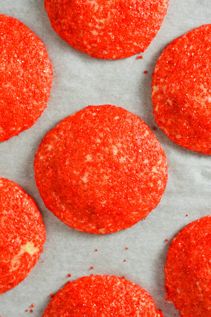 Vibrant red sprinkles adorn some Peppermint Sprinkle Cookies, sitting on a parchment paper lined cookie sheet.