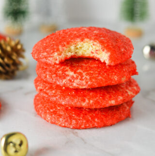 A stack of Peppermint Sprinkle Cookies with some bells, pinecones and small Christmas trees in the background, giving them a cozy and festive feel.