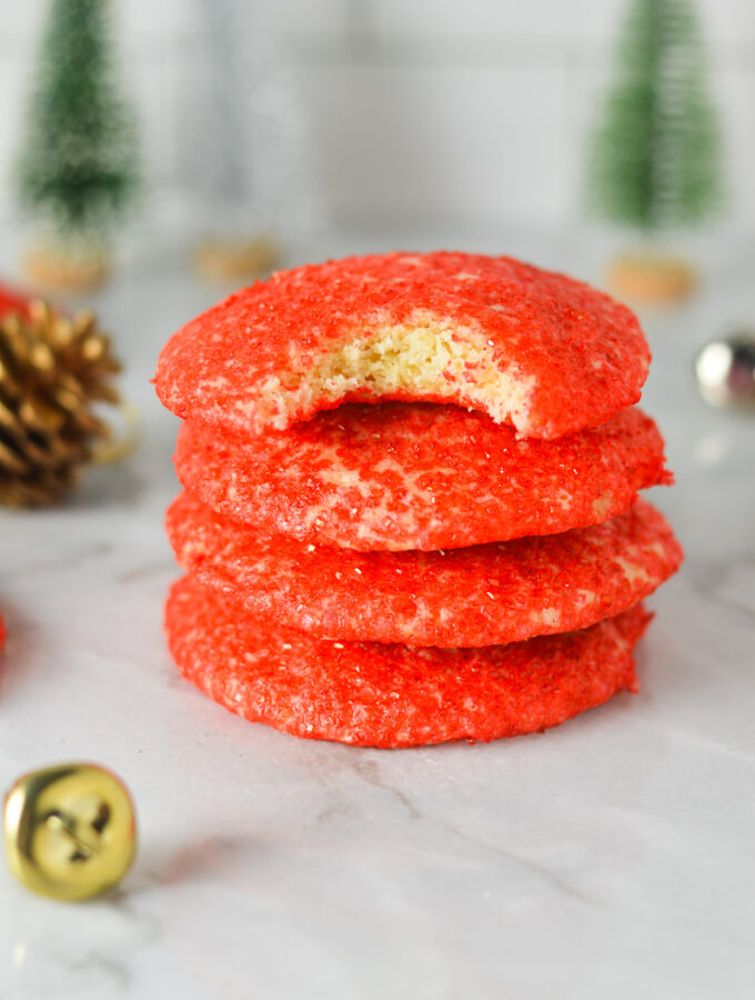 A stack of Peppermint Sprinkle Cookies with some bells, pinecones and small Christmas trees in the background, giving them a cozy and festive feel.