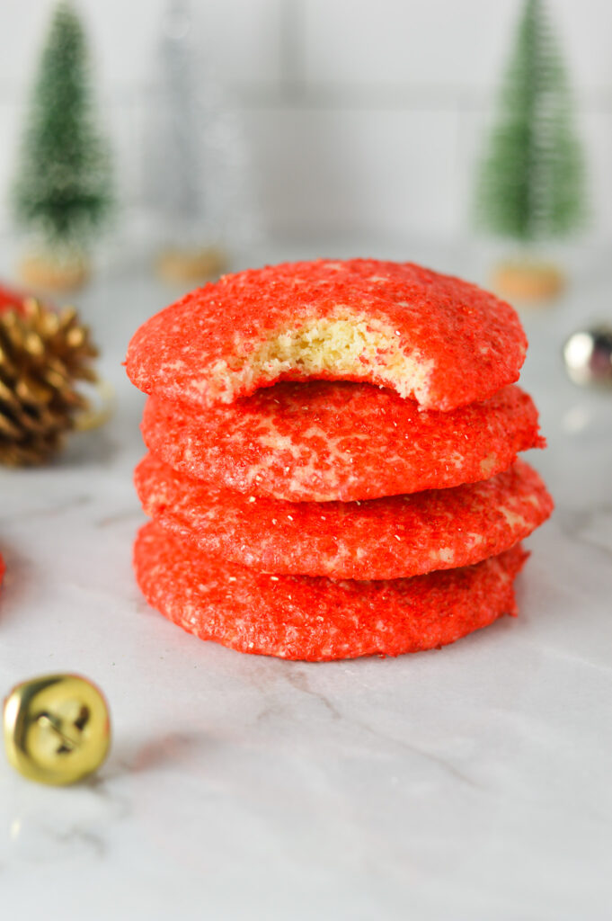 A stack of Peppermint Sprinkle Cookies with some bells, pinecones and small Christmas trees in the background, giving them a cozy and festive feel.