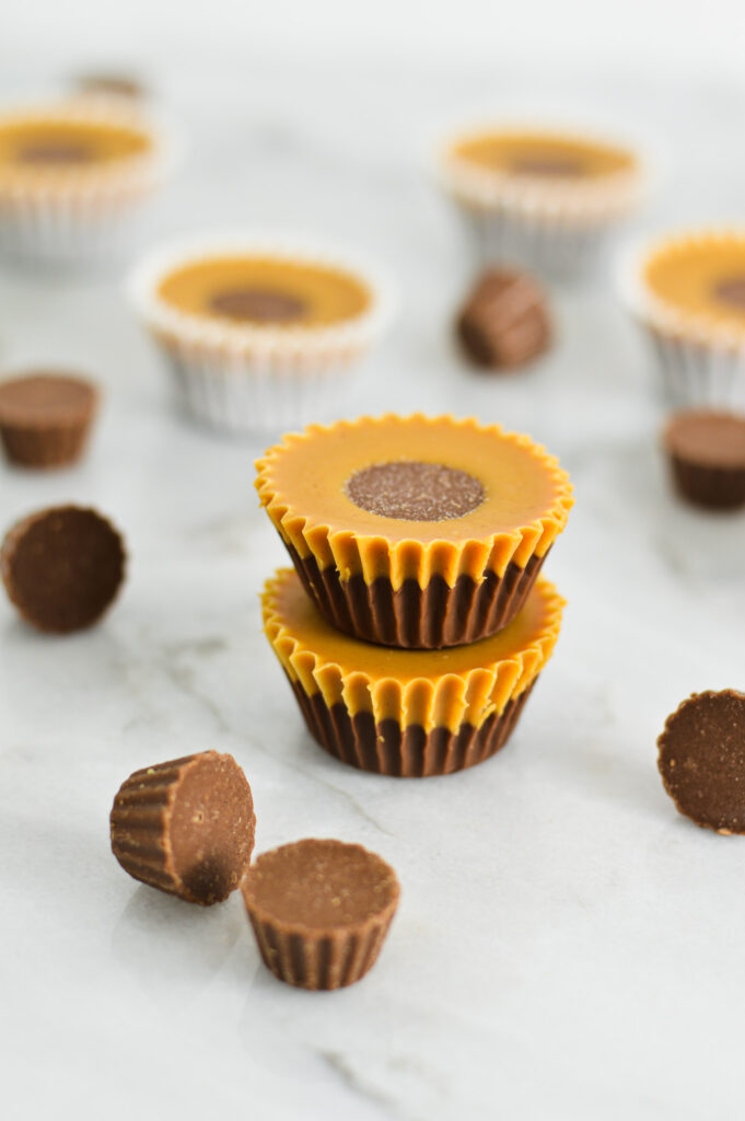 Two Reese's Peanut Butter Nutella Cups stacked on top of each other, with mini Reese's Peanut Butter cups scattered around it.