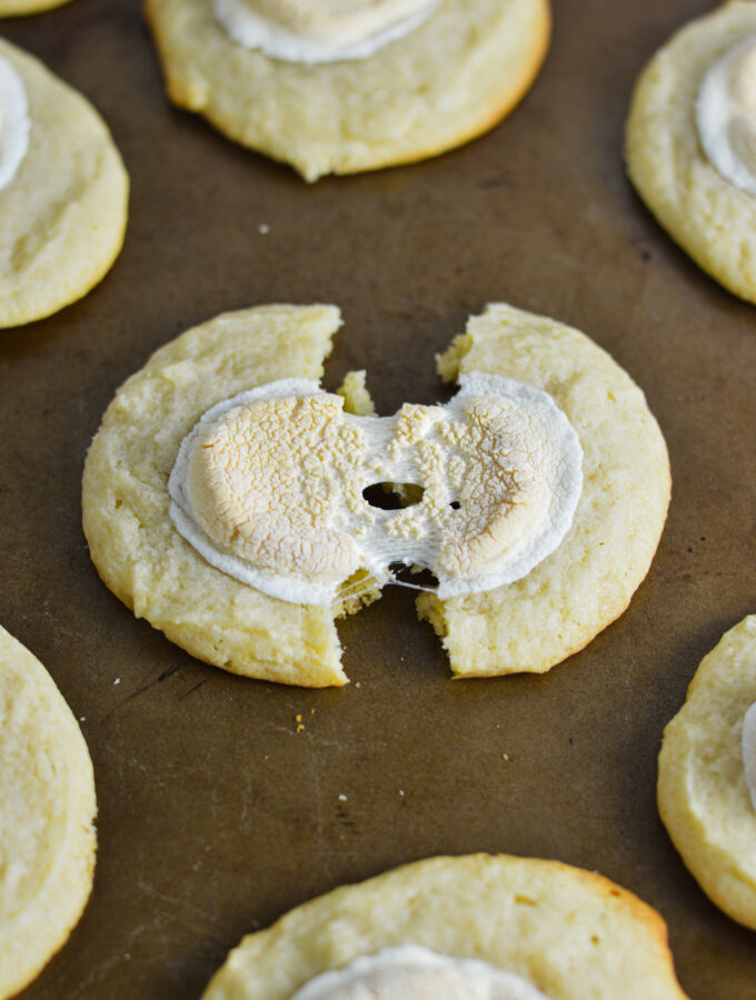 White Hot Chocolate Cookies on a cookie sheet, with a cookie cut in half showing the melted marshmallow topping.