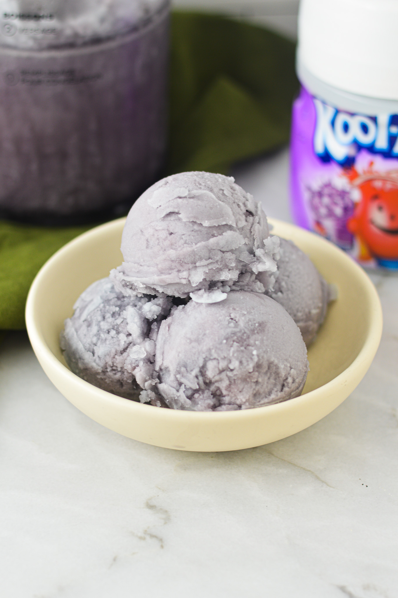 Vibrant purple Ninja Creami Kool-Aid Italian Ice with a container of grape kool aid in the background.