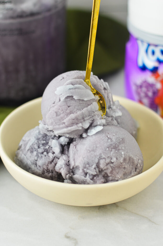 A small bowl of violet Ninja Creami Kool-Aid Italian Ice with a golden spoon sticking out of the top.