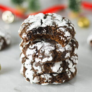 A stack of Peppermint Chocolate Crinkle Cookies with a bite taken out of the top one, revealing a fudgy interior.