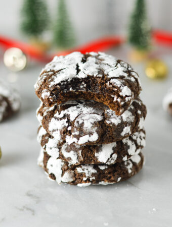 A stack of Peppermint Chocolate Crinkle Cookies with a bite taken out of the top one, revealing a fudgy interior.