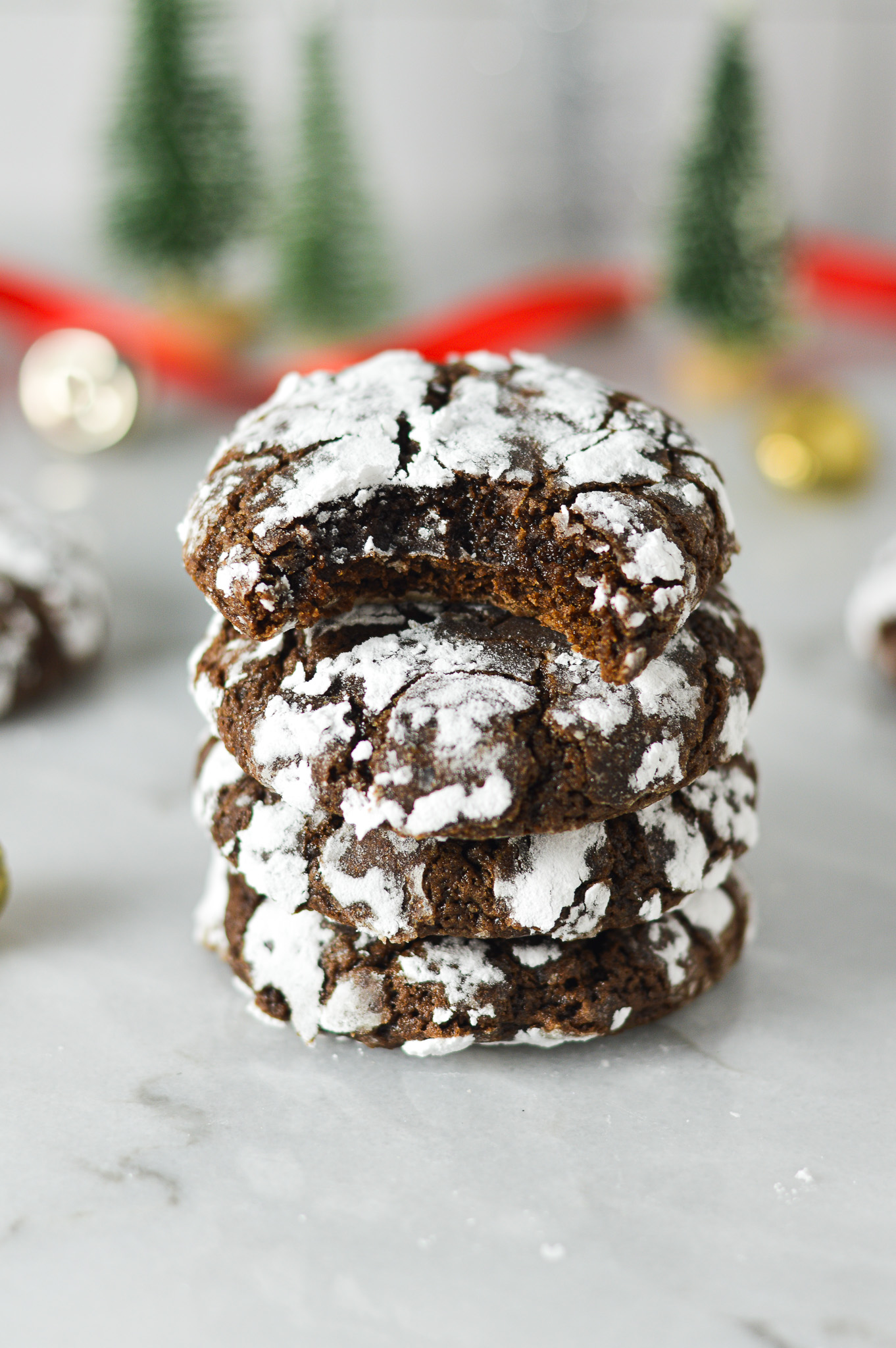 A stack of Peppermint Chocolate Crinkle Cookies with a bite taken out of the top one, revealing a fudgy interior.