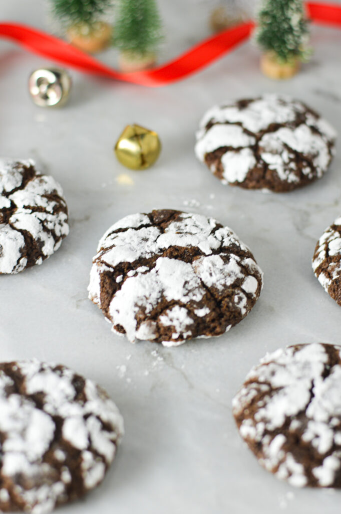 Peppermint Chocolate Crinkle Cookies on a granite surface surrounded by holiday decor, giving it a festive treat feel.