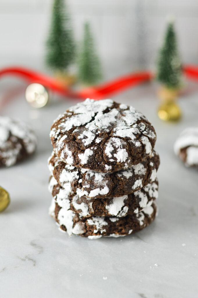 A stack of Peppermint Chocolate Crinkle Cookies surrounded by Christmas decor, giving it a holiday treat feel.