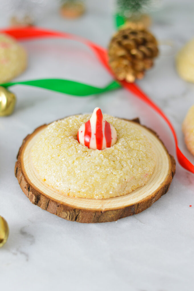 A Peppermint Kiss Cookie on top of a wooden coaster, with red and green ribbon in the background giving it a festive feel.