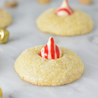 Peppermint Kiss Cookies with a red and white striped peppermint kiss on top of fluffy sanding sugar coated cookies. There are bells in the background, adding to the Christmas feel.