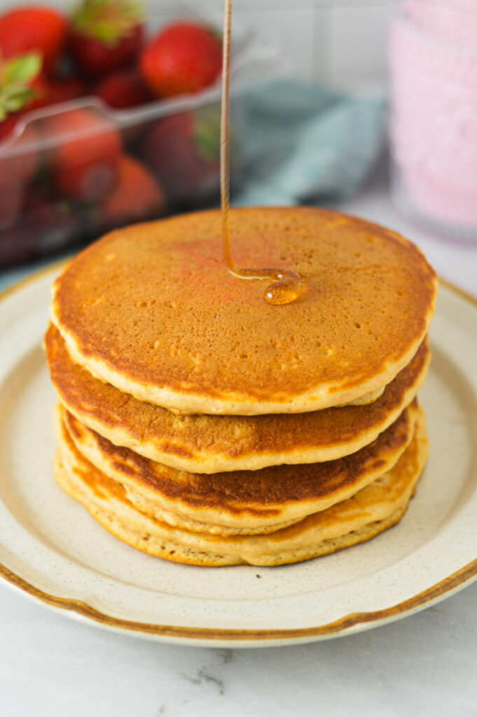 A stack of soft pink Strawberry Milk Pancakes with maple syrup being drizzled on top.