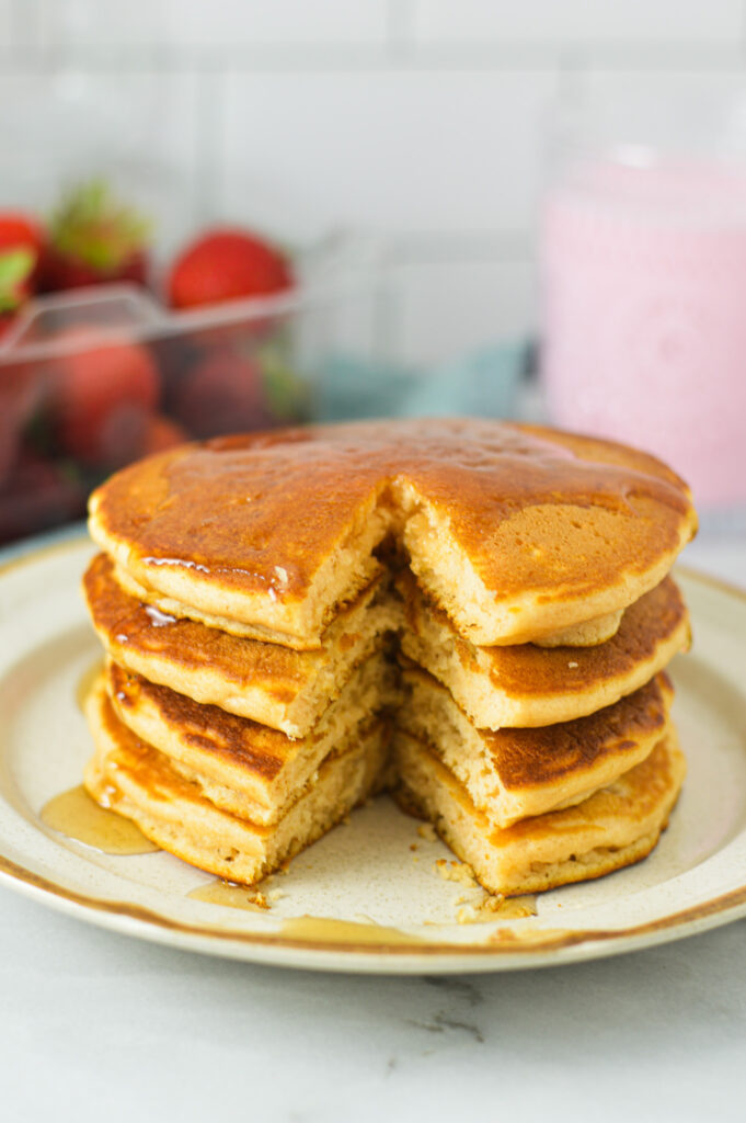 A stack of fluffy Strawberry Milk Pancakes, with a wedge like slice taken out to show its soft interior.