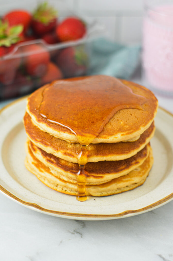 A stack of soft Strawberry Milk Pancakes, with a drizzle of maple syrup dripping down the sides.