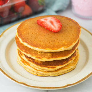 A stack of Strawberry Milk Pancakes on a small plate, topped with sliced fresh strawberries.