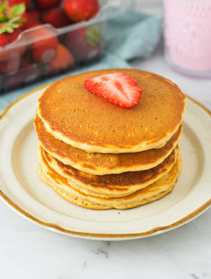 A stack of Strawberry Milk Pancakes on a small plate, topped with sliced fresh strawberries.