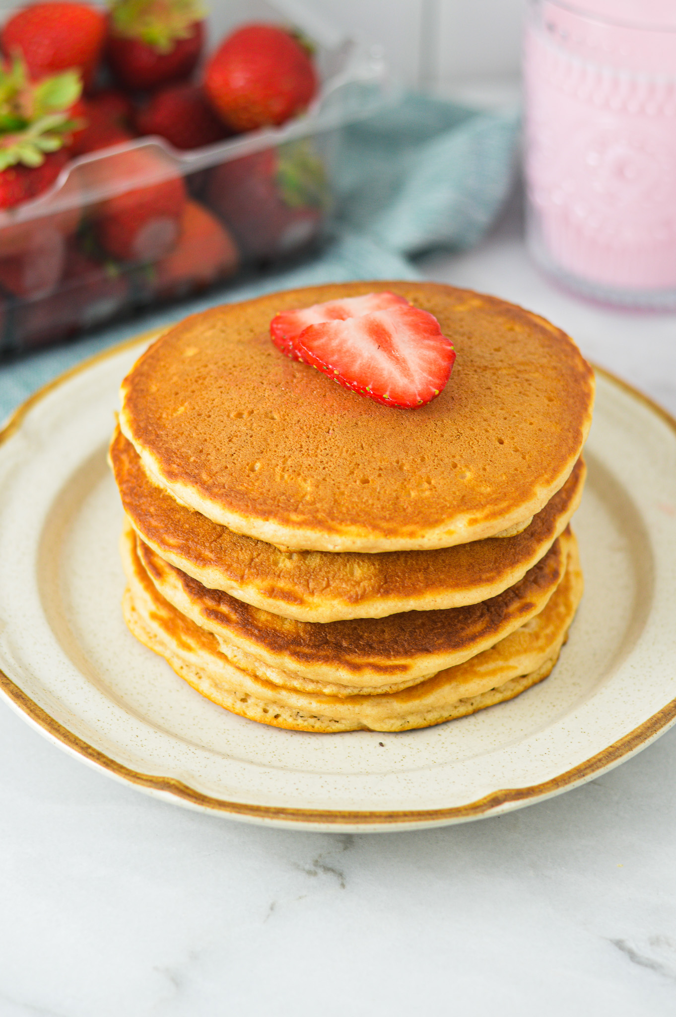 A stack of Strawberry Milk Pancakes on a small plate, topped with sliced fresh strawberries.