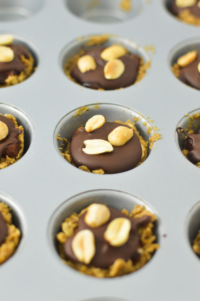 Mini Vegan Protein Snickers Cups in a mini muffin pan. The tops of the melted chocolate and peanuts are visible.