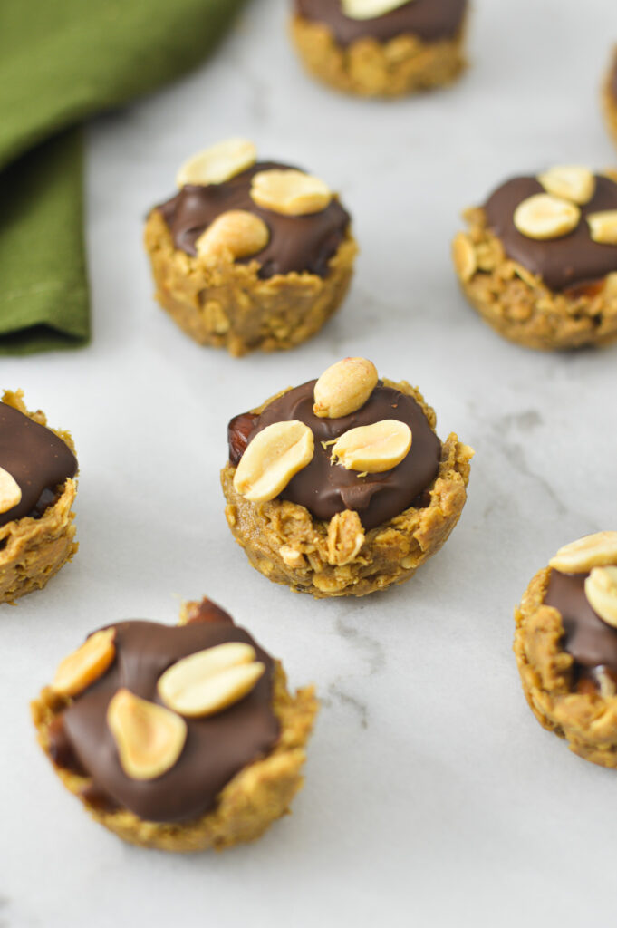 Hearty Mini Vegan Protein Snickers Cups on a granite surface. The oat mixture base gives the cups a rustic feel alongside the chocolate coating and peanuts on top.