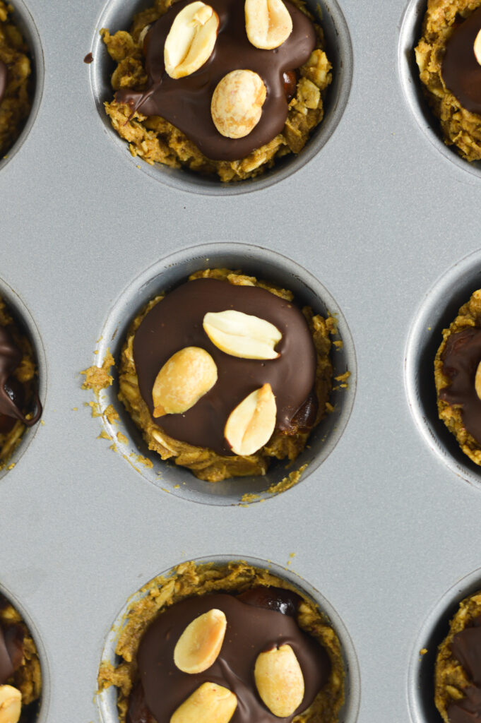 An overhead shot of Mini Vegan Protein Snickers Cups in a mini muffin tin, with the melted chocolate and dry roasted peanuts visible.