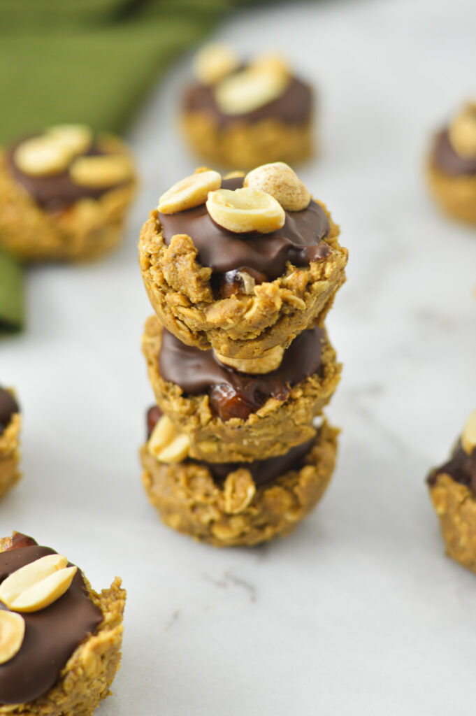 A stack of Mini Vegan Protein Snickers Cups, with the oat mixture, dates, melted chocolate and peanut layers all clearly visible.