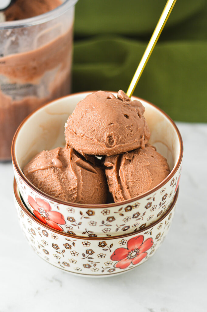 Scoops of Ninja Creami Lite Chocolate Pudding Ice Cream inside a small bowl, with a small golden spoon sticking out of the homemade ice cream.