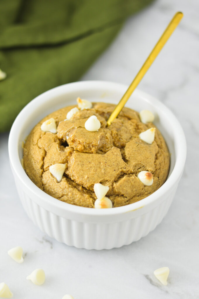 White Chocolate Protein Blended Baked Oats in a white ramekin with a gold spoon sticking out of the center.